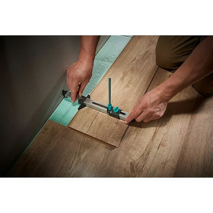 Wolfcraft Anreißlehre - Länge: 295 mm - Person verwendet Wolfcraft Laminat- und Parkettverlegewerkzeug, um ein Laminatstück am Wandrand anzupassen und zuzuschneiden.