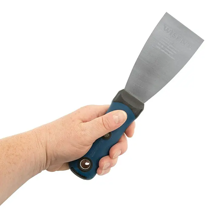 Wisent Malerspachtel mit Softgriff - Klingenbreite: 60 mm - Nahaufnahme einer Hand, die einen blauen Spachtel hält, ein vielseitiges Werkzeug für Bau- und Renovierungsarbeiten, ideal zum Glätten oder Abkratzen von Oberflächen.