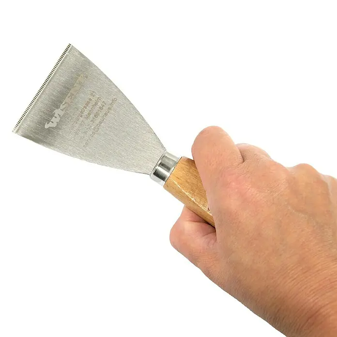 Wisent Entrosterspachtel - Klingenbreite: 60 mm, Länge: 180 mm - Nahaufnahme einer Hand, die einen scharfen Spachtel mit Holzgriff hält, ein Werkzeug für Präzisionsarbeiten.