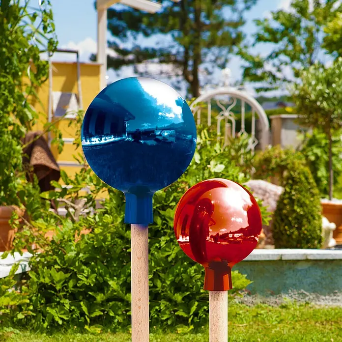 Windhager Glaskugel - Durchmesser: 16 cm, Blau - Nahaufnahme von zwei Gartenkugeln, eine blau und eine rot, die auf Holzstäben im Garten stehen und die Umgebung reflektieren.