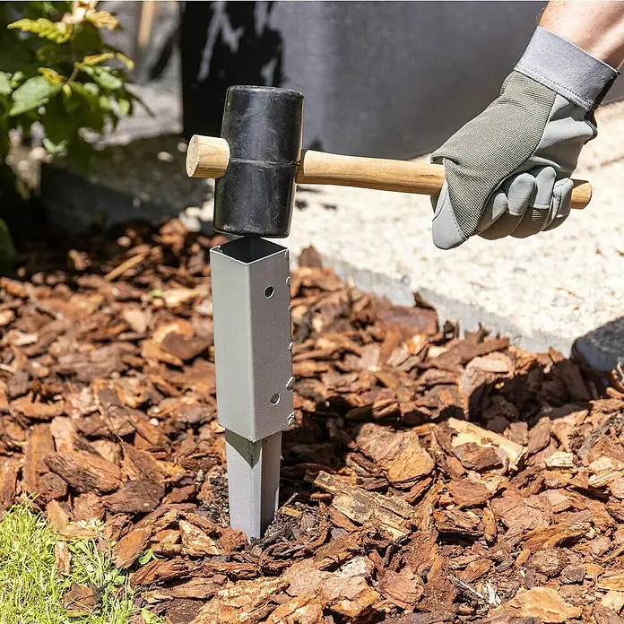 Rankhilfe - B x H: 70 x 119 cm, Holz, Braun - Ein grauer Erdanker wird mit einem Hammer in den Boden getrieben, um Stabilität zu gewährleisten. Ideal für Gartenprojekte.