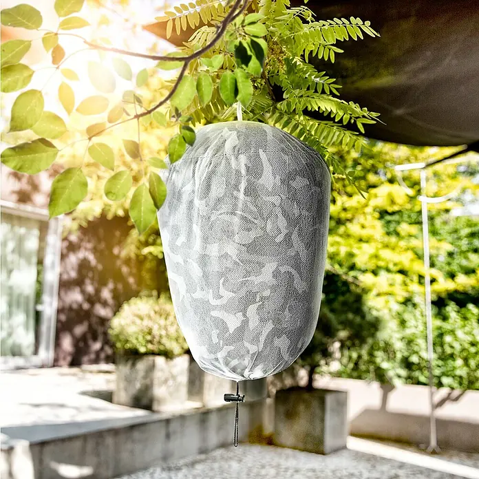 Windhager Wespennest Attrappe Wasp Away - 20 x 20 x 35 cm - Eine Pflanze ist mit einem camouflagefarbenen Pflanzensack überzogen, der am Baum hängt und Schutz vor Kälte und Wind bietet.