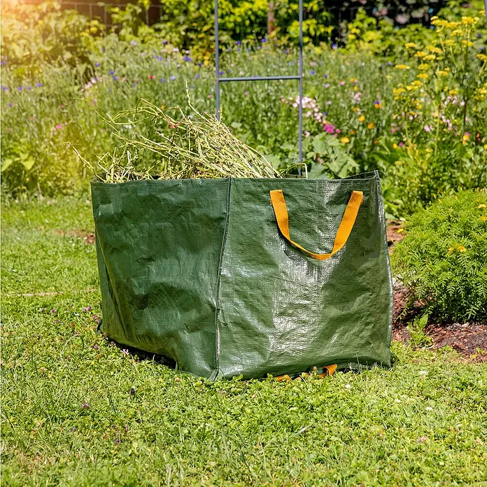Windhager Gartenabfallsack Bigload - Fassungsvermögen: 225 l, Grün - Gartensack gefüllt mit Gartenabfällen auf Rasen mit Blumen im Hintergrund. Der grüne Sack hat gelbe Griffe.