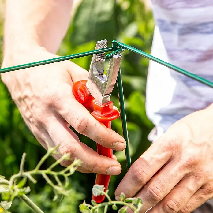 Windhager Rankhilfe Tomaten-Turm - L x B x H: 118 x 35 x 35 cm, Dunkelgrün - Nahaufnahme einer Person, die mit einer roten Zange grünen Draht befestigt, wahrscheinlich im Gartenbau oder zur Pflanzenunterstützung.