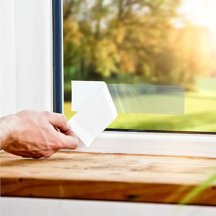 Windhager Fliegenfalle Fenster - 4 Stk. - Ein Mann bringt eine transparente Fensterfolie an, um die Wärmeisolierung zu verbessern. Die Folie schützt vor Wärmeverlust und spart Energie.