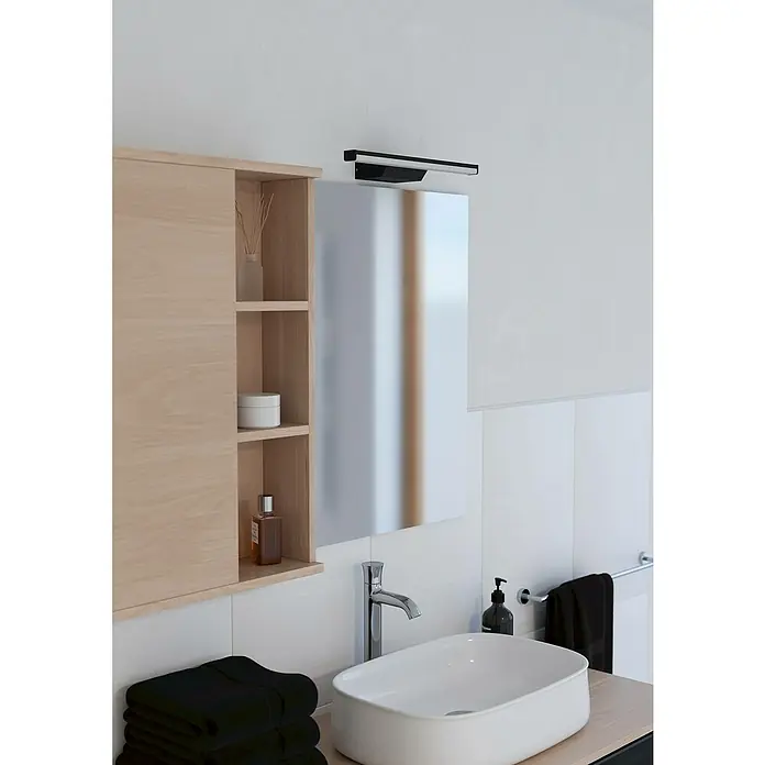 Eglo connect.z LED-Spiegelleuchte Regello-Z - 12 W, L x B x H: 60 x 13 x 4 cm, Schwarz, RGBW - Badezimmer-Interieur mit Waschtisch, Spiegel mit Beleuchtung und einem Holzregal. Schwarze Handtücher und eine Seife ergänzen das moderne Design.