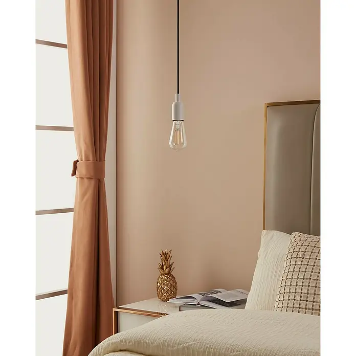 Eglo connect.z Smart-LED-Lampe ST64 - E27, Dimmbar, Warmweiß, 806 lm, 6 W - Eine einzelne Glühbirne hängt an einem schwarzen Kabel über einem Bett. Sie erhellt das Schlafzimmer mit warmem Licht.