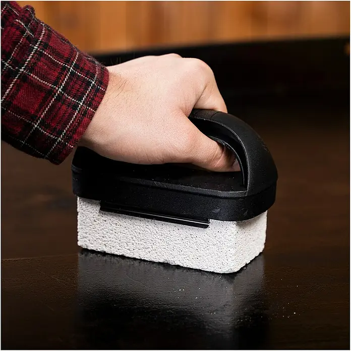 Blackstone Limpiador para parrillas - 8 pzs., Acero inoxidable - Se muestra un ladrillo limpiador de parrillas manual que se utiliza para fregar una superficie de plancha.