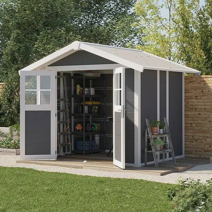 Grosfillex Caseta para jardín Deco - Medidas ext. (An x Pr): 295 x 261 cm, Plástico, Gris oscuro, 4,9 m² - Imagen de una caseta de jardín gris con bordes blancos y puertas abiertas, situada sobre una plataforma de madera en un jardín.