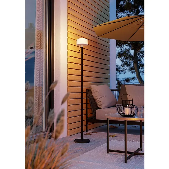 Eglo Solar-Stehleuchte Montapalma-L - Schwarz, IP44, Ø x H: 15 x 140 cm - Elegante schwarze Stehlampe mit zylindrischem Lampenschirm beleuchtet stilvoll eine Terrasse mit Sitzbereich und Sonnenschirm.