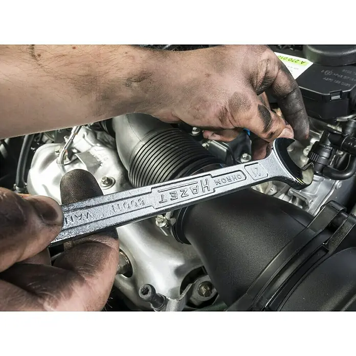 Hazet Ringmaulschlüssel 8Schlüsselweite: 8 mm, 15 ° abgewinkelt, DIN 3113 A - Nahaufnahme von Händen, die mit einem HAZET-Schraubenschlüssel an einem Automotor arbeiten. Fokus auf den Schraubenschlüssel und die Motorbauteile.