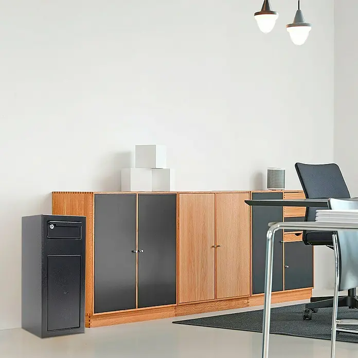Rottner Einwurftresor Cashmatic 1 - 26 x 25 x 60 cm, Doppelbartschloss - Das Bild zeigt einen schwarzen Safelock-Briefkasten neben einem Sideboard, das in einem modernen Büroraum steht.