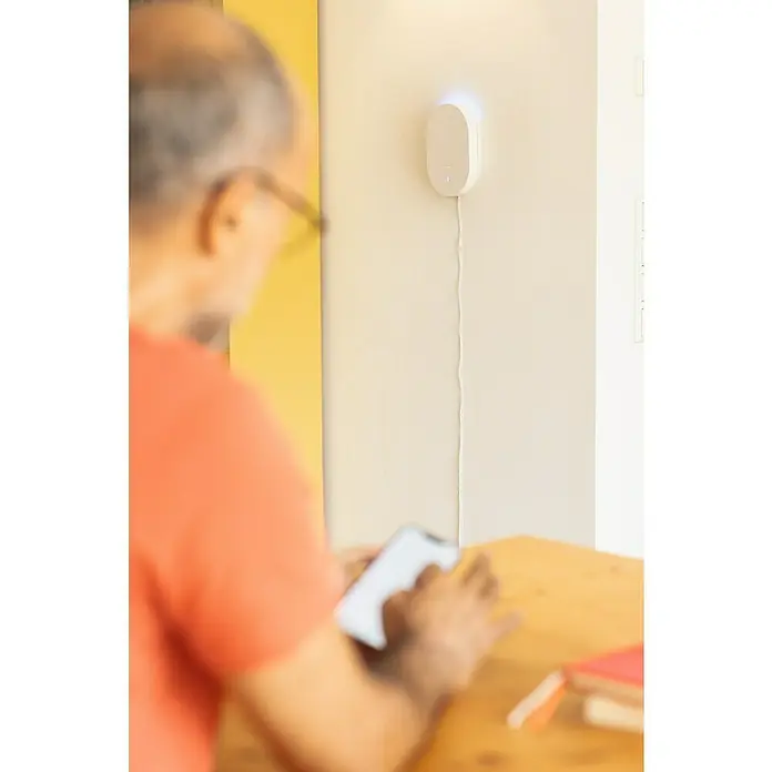 Abus Alarmanlagen-Set Smartvest Pro FUAA45000 - Akustischer Alarm - Ein ovaler, weißer Luftreiniger hängt an der Wand und verbessert die Luftqualität. Das Gerät ist mit einem Stromkabel verbunden.