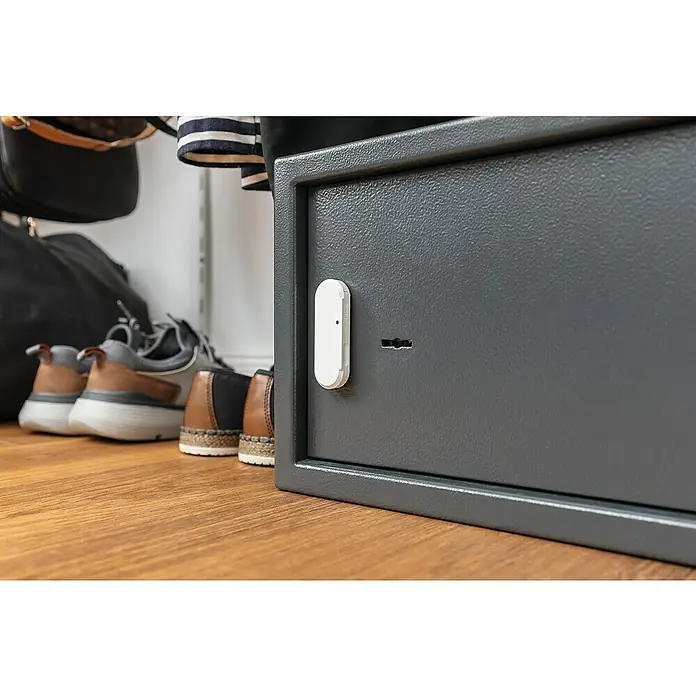 Abus Erschütterungssensor Smartvest Pro FUEM45000 - Reichweite ca.: 100 m - Ein grauer Safe mit einem weißen Sensor in einem Schrank, der zusätzliche Sicherheit bietet. Die Kombination aus sicherem Tresor und Sensor garantiert zusätzlichen Schutz.