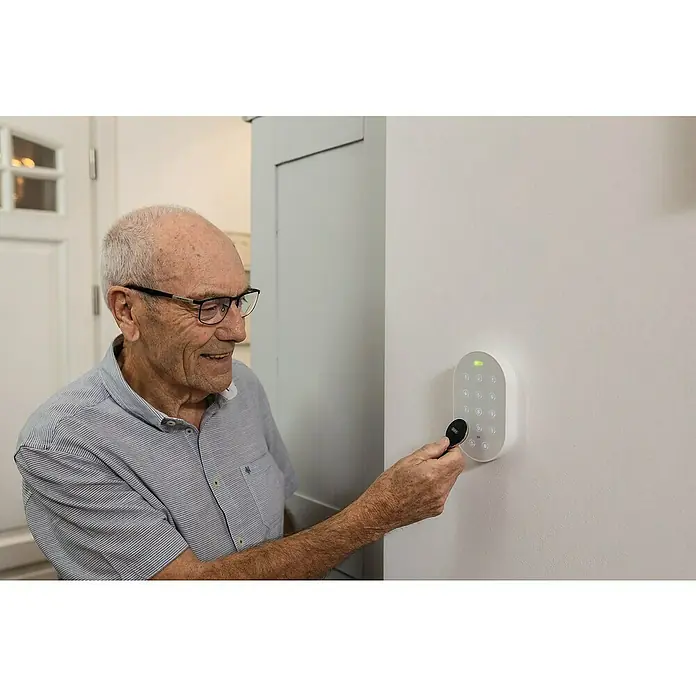 Abus RFID-Badge ID Schlüsselanhänger Smartvest Pro FUPC45000 - Passend für: Funk-Alarmanlage Smartvest Pro, 30 mm - Ein älterer Mann bedient ein smartes Türschloss mit einem Schlüsselanhänger. Das moderne Schloss verfügt über ein Tastenfeld und ein schlankes Design.
