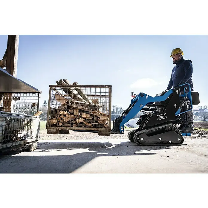 Scheppach Palettengabel - Passend für: Scheppach Kompaktlader MKL730 - Scheppach Minilader mit einem Arbeiter beim Heben eines Holzkorbs. Der Lader ist blau und schwarz, ideal für schwere Lasten.
