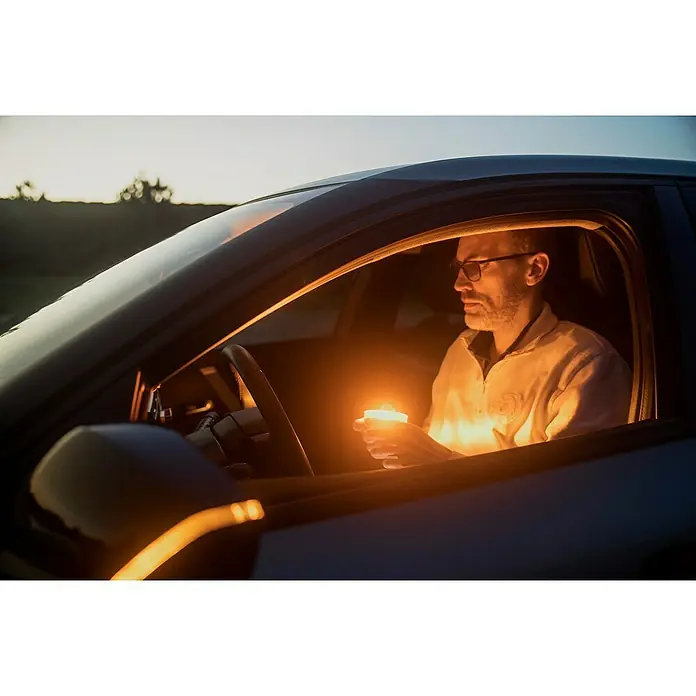 Luz de emergencia Help Flash IoT+ - Apto para: Avería en el vehículo - Hombre en coche sosteniendo una vela. La cálida luz de las velas ilumina el interior del vehículo, proyectando un suave resplandor en el rostro del hombre.