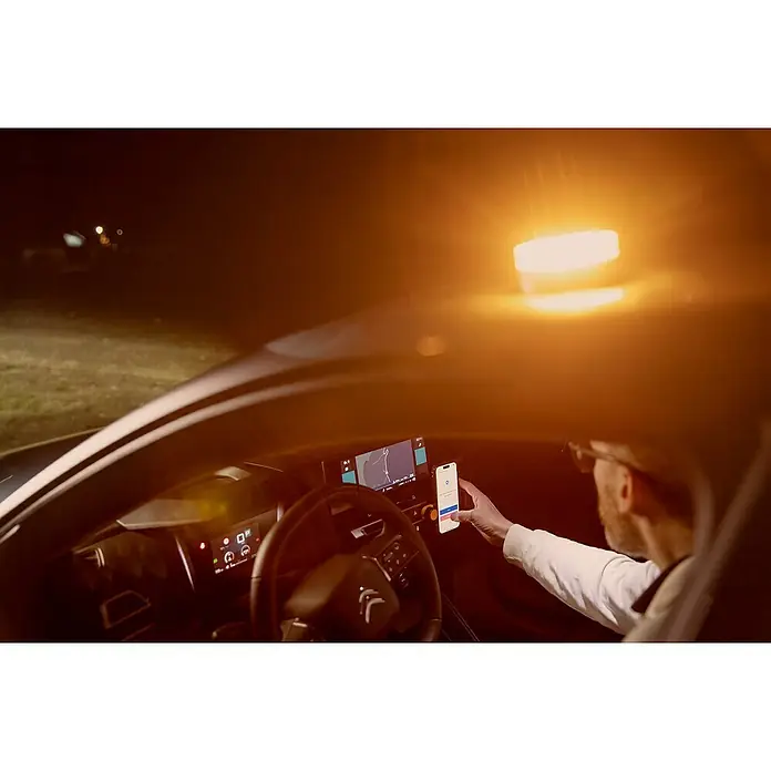 Luz de emergencia Help Flash IoT+ - Apto para: Avería en el vehículo - Un hombre en el coche opera un teléfono inteligente conectado a un soporte magnético, con la navegación en ejecución en la pantalla.