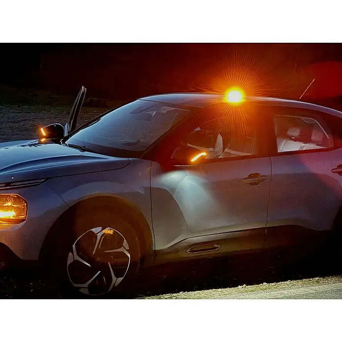 Luz de emergencia Help Flash IoT+ - Apto para: Avería en el vehículo - Primer plano de un coche moderno con una llamativa luz naranja en el techo, iluminando el entorno oscuro.