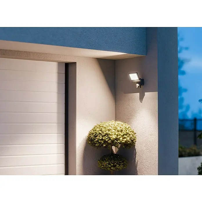 Steinel LED-Strahler CAM 2 SC - 21 W, 2.310 lm, 3.000 K, IP44 - Moderne Außenleuchte an einer Hauswand montiert, die einen Gartenbaum beleuchtet. Die Leuchte sorgt für ein helles, gerichtetes Licht.