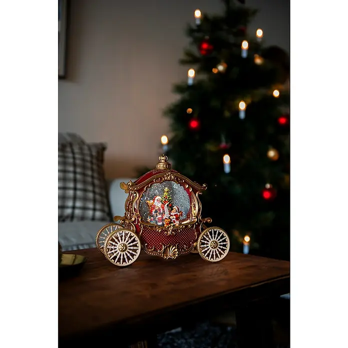 Konstsmide LED-Schneelaterne Kutsche - Innen, Rot, 26 x 11,5 x 22,6 cm, Batteriebetrieben - Weihnachtliche Kutsche Schneekugel mit Santa, Baum und Teddy auf einem Holztisch mit Weihnachtsbaum im Hintergrund.