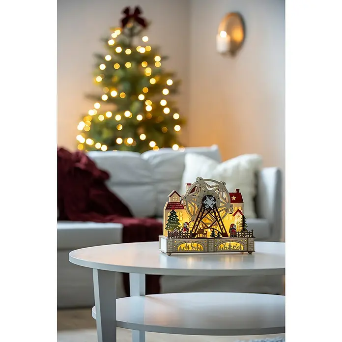 Konstsmide LED-Szenerie Weihnachtsmarkt - L x B x H: 28 x 12 x 24,5 cm, Weiß, Batteriebetrieben, LED - Weihnachtliche Szene mit einem beleuchteten hölzernen Riesenrad auf einem Tisch, ein festlich geschmückter Baum im Hintergrund sorgt für Stimmung.