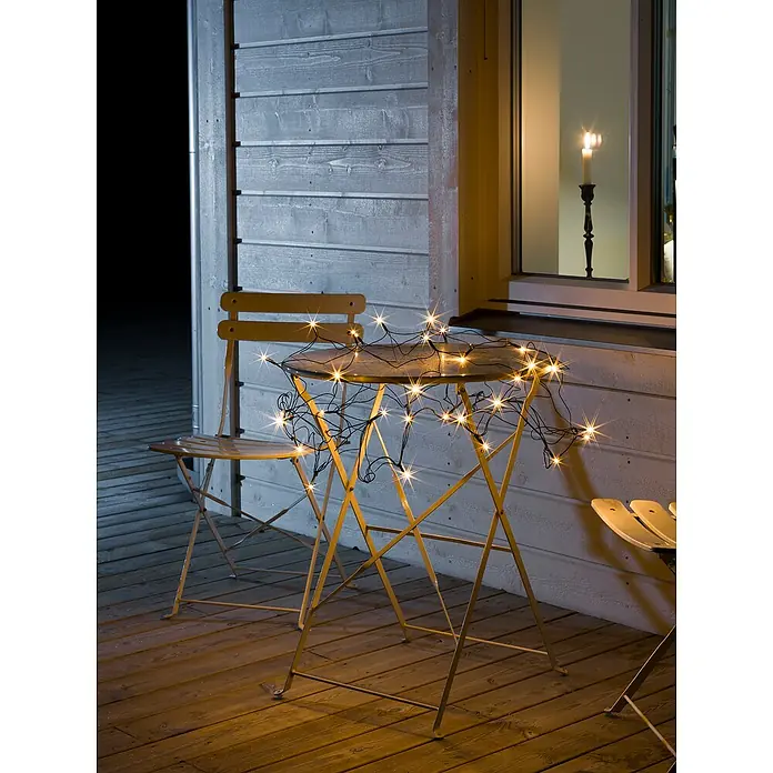 Konstsmide LED-Lichtnetz - Außen, Lichtfarbe: Bernstein, Netzbetrieben - Lichterketten auf einem Tisch und Stuhl, schaffen eine warme Atmosphäre auf der Terrasse.
