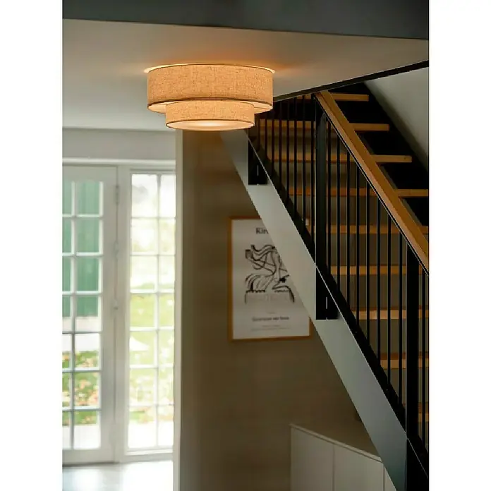 Nordlux Plafón redondo Malodin - 40 W, Ø x Al: 50 x 22 cm, Beige, E27 - Una lámpara de techo de tela de dos niveles cuelga en un pasillo con escaleras. La luz cálida ilumina suavemente el espacio.