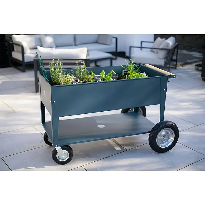 Herstera Garden Kräuterhochbeet Swivel - L x B x H: 120 x 60 x 84 cm, Anthrazit - Ein rollender Kräutergartenwagen mit verschiedenen Kräutern in einem Außenbereich mit Gartenmöbeln im Hintergrund.