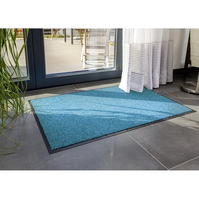 Astra Schmutzfangmatte Diamant - Türkis, 40 x 60 cm, Material Nutzschicht: 100 % Polyamid - Eine türkisfarbene Schmutzfangmatte mit schwarzem Rand liegt vor einer Terrassentür auf dunklen Fliesen.