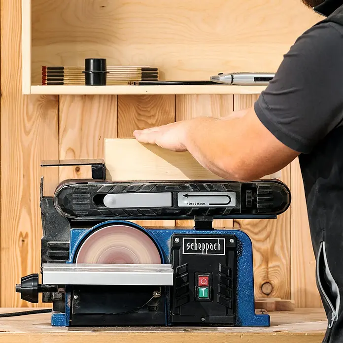 Scheppach Band- & Tellerschleifer BTS900 - 370 W, 2.850 U/min - Nahaufnahme einer Scheppach Kombi-Schleifmaschine im Einsatz mit Schleifband und Schleifscheibe zum Bearbeiten eines Holzstücks.