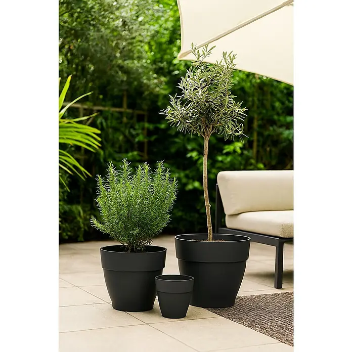 Elho Vibia Campana Maceta para planta Vibia Campana - Dimensiones externas (Ø x Al): 39 x 33,4 cm, Plástico, Antracita - Tres macetas negras con plantas están en un patio, con una silla y una sombrilla al fondo.