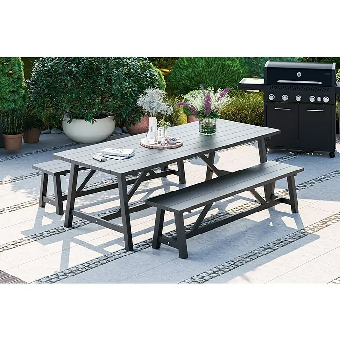 Sunfun Melina Gartenbank - B x T x H: 190 x 42,4 x 45,7 cm, Akazie, Black Washed - Ein graues Gartentisch-Set mit Bänken und einem Grill im Hintergrund, perfekt für Mahlzeiten im Freien.