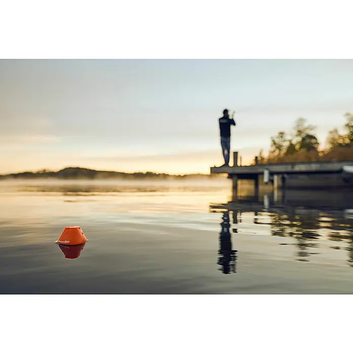 Deeper Fishfinder Start - Höhe: 58 mm, WLAN - Das orangefarbene Bojenstartgerät schwimmt im Wasser und reflektiert sich. Im Hintergrund steht eine Person auf einem Steg am See.