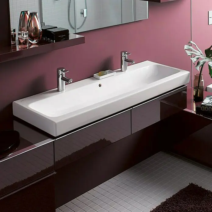 Geberit iCon Doppelwaschtisch - 120 x 48,5 cm, Ohne Spezialglasur, Hahnloch: Mitte, Mit Überlauf, Weiß - Das Bild zeigt ein modernes Badezimmer mit einem rechteckigen, weißen Doppelwaschbecken und zwei Armaturen auf einem dunklen Unterschrank.