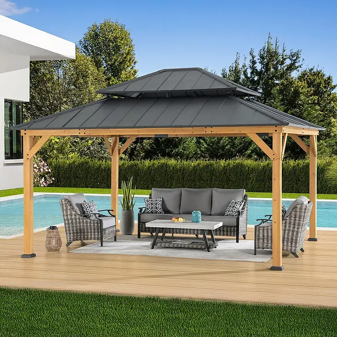 Sunjoy Pavillon Rimo - L x B: 390 x 450 cm, Farbe Dach: Anthrazit - Bild eines Pavillons mit Holzrahmen und grauem Dach über einer grauen Sofagarnitur mit Couchtisch auf einer Holzterrasse am Pool.
