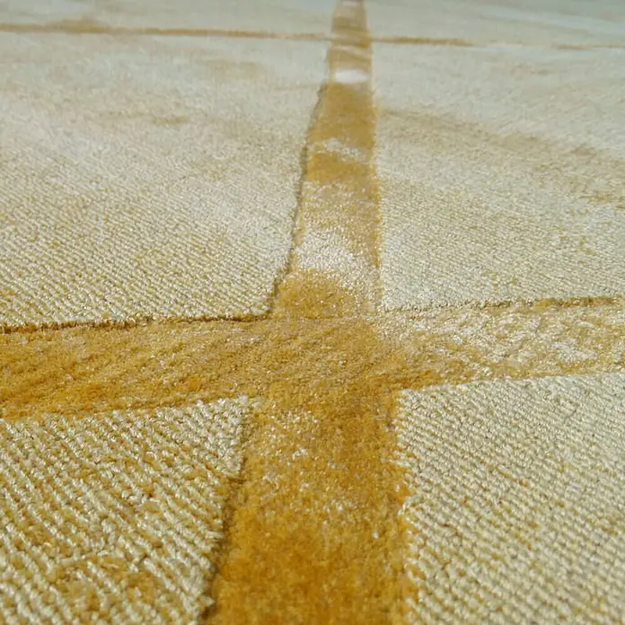 Kayoom Kurzflorteppich Luxury 210 - Gelb, 290 x 200 cm, 100 % Viskose - Nahaufnahme eines beigen Teppichs mit einem goldenen Kreuzmuster. Das schlichte Design und die Textur verleihen dem Teppich Wärme und Charakter.
