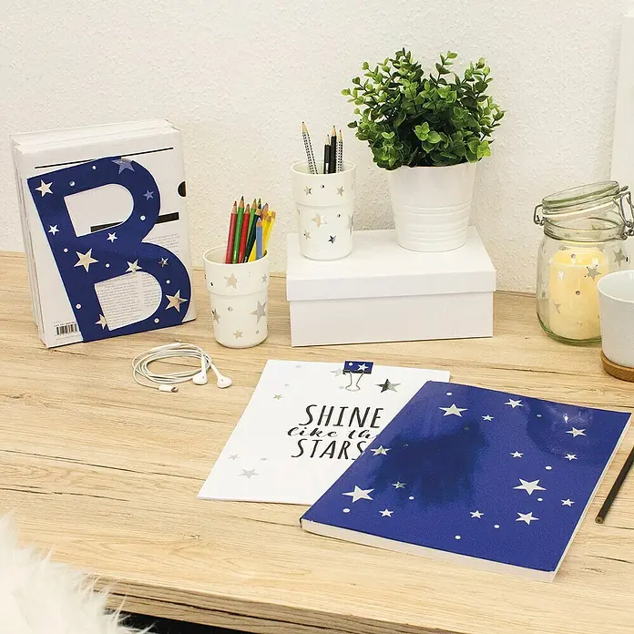 D-c-fix Klebefolie Uni Lack - 200 x 45 cm, Royal Blau, Selbstklebend - Eine Schreibtischszene mit Schreibwaren, darunter Notizbücher, Stiftehalter und einer Pflanze, die eine Sternenmotive aufweisen.