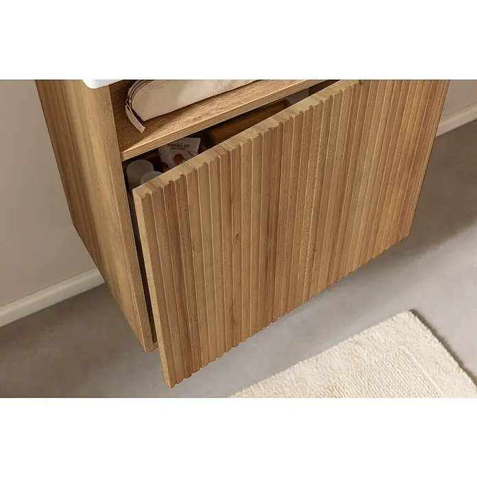 Camargue Pure Badmöbel-Set - Gesamtbreite Badmöbel: 55 cm, Berg Eiche, Matt - Ein Badezimmerschrank mit einer offenen, geriffelten Holztür, der einen Einblick in den Stauraum mit Pflegeprodukten bietet.