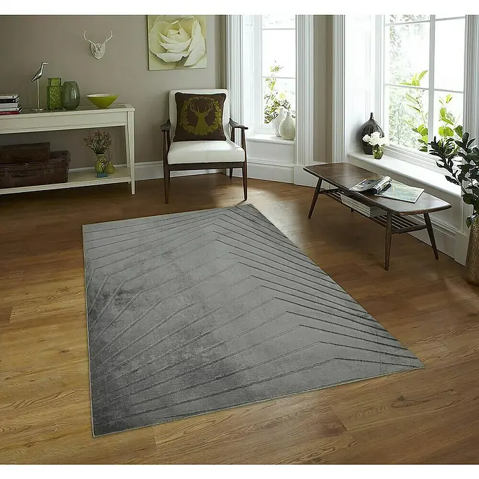 Alfombra de pelo corto Stelvio Picos - Gris, 230 x 160 cm, 100% Poliéster - Una alfombra gris con un patrón geométrico en zigzag sobre un suelo de madera en una sala de estar luminosa, añadiendo un toque moderno al espacio.