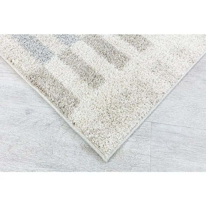 Alfombra de pelo largo Rayas - Natural, 230 x 160 cm, 100% Polipropileno - Primer plano de una alfombra con un diseño abstracto en tonos neutros, colocada sobre un suelo de madera clara, creando un ambiente acogedor.