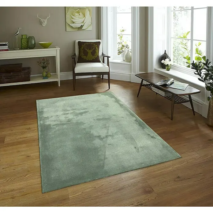 Alfombra de pelo corto Toscana - Verde, 230 x 160 cm, 100% Poliéster - Una alfombra verde reposa sobre un suelo de madera en una acogedora sala de estar, añadiendo un toque de elegancia y confort al espacio.