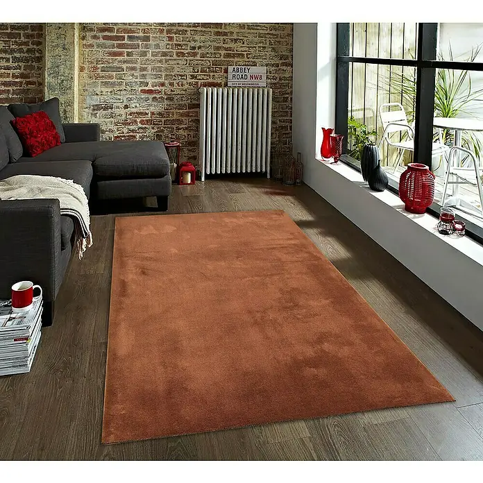 Alfombra de pelo corto Toscana - Teja, 110 x 60 cm, 100% Poliéster, Antideslizante - Una alfombra beige en una sala de estar con un sofá gris, una pared de ladrillo y una gran ventana.