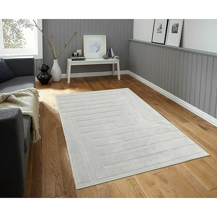 Alfombra de pelo corto Stelvio Cuadros - Plata, 230 x 160 cm, 100% Poliéster - Una alfombra gris con un patrón geométrico se muestra sobre un piso de madera en una elegante sala de estar.
