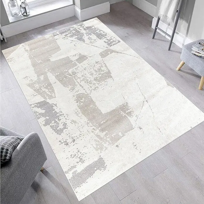 Alfombra de pelo corto Brochazos - Natural, 110 x 60 cm, 100% Poliéster - Una alfombra rectangular con un patrón abstracto en tonos grises y beige se encuentra sobre un suelo de madera clara. La alfombra es el centro.