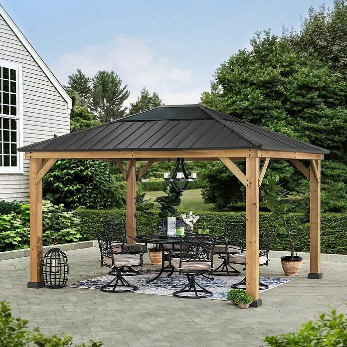 Sunjoy Pavillon Bruri - L x B: 394 x 336 cm, Farbe Dach: Anthrazit - Eleganter Pavillon mit Holzbalken und schwarzem Metalldach über einer stilvollen Gartengarnitur auf einer gepflasterten Terrasse.