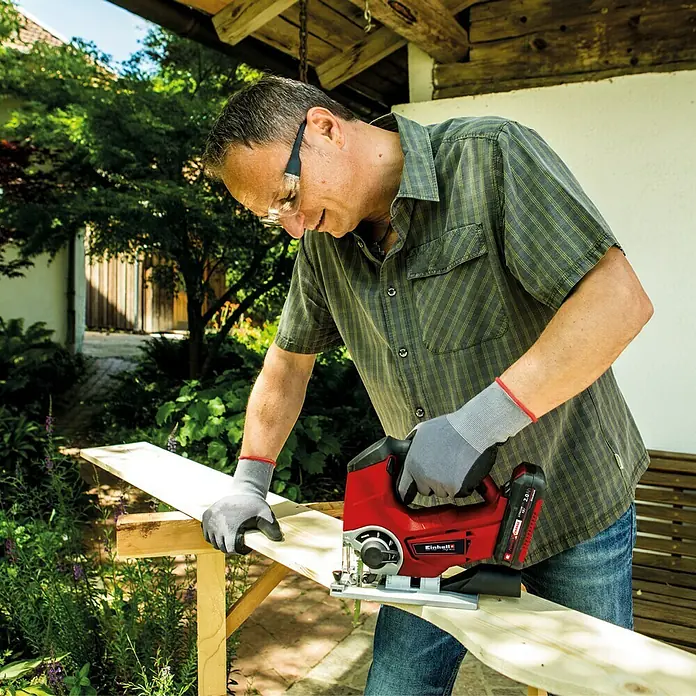 Einhell Power X-Change 18V Akku-Pendelhubstichsäge TE-JS 18/80 Li-Solo - 18 V, Ohne Akku, 0 /min - 2.400 /min - Ein Mann sägt mit einer Einhell Akku-Stichsäge ein Brett im Freien. Die Stichsäge ist rot und schwarz und hat einen Akku.