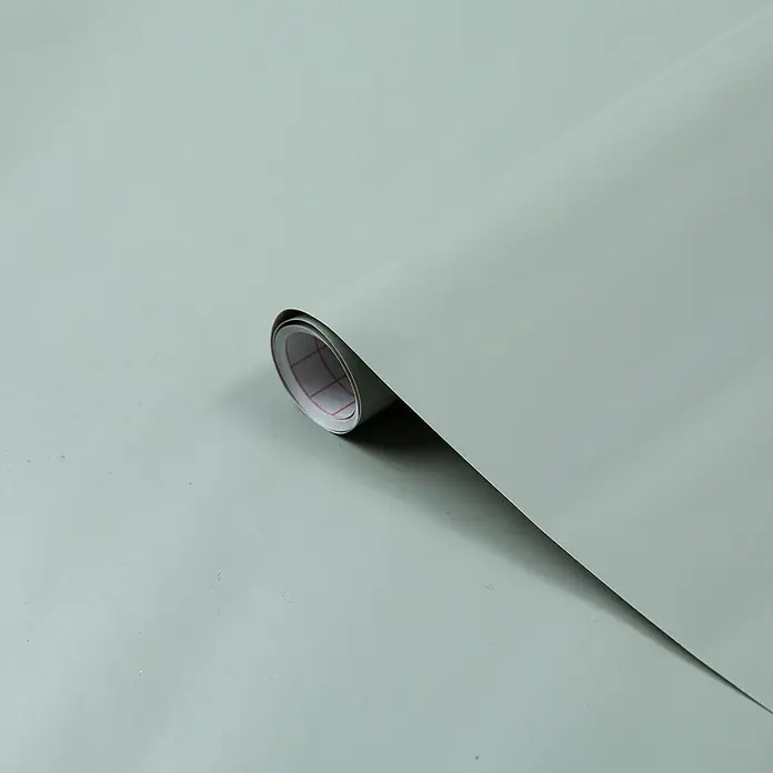 D-c-fix Dekorfolie Seidenmatt - 67,5 x 200 cm, Grün - Nahaufnahme einer Rolle grauer selbstklebender Vinylfolie, teilweise abgerollt, mit sichtbarem Gittermuster auf der Rückseite.