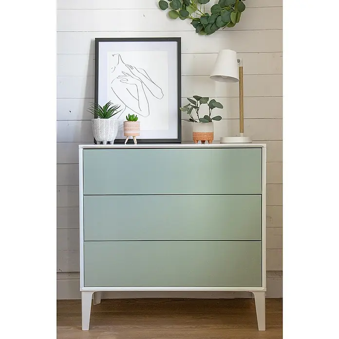 D-c-fix Dekorfolie Seidenmatt - 67,5 x 200 cm, Grün - Stilvolle mintgrüne Kommode mit drei Schubladen, dekoriert mit Pflanzen, einem Bild und einer Lampe, die eine harmonische und moderne Atmosphäre schaffen.