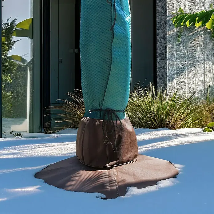 BioGreen Winterschutz Wurzelschutz für Palmen - 100 x 30 cm - Ein Pflanzensack in Braun und Blau schützt eine Pflanze im Winter vor Schnee und Kälte im Garten.